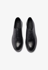 Black leather lace-up shoes with a smooth finish, rounded toe, and contrasting white sole trim. Features minimal stitching and logo inside.