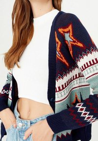 Strickjacke in Marineblau mit bunten, geometrischen Sternen und Zickzackmustern. Hat einen Knopfverschluss und gerippte Bündchen für mehr Textur.