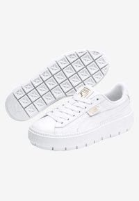 Bílé platformové tenisky s texturovanými detaily a zlatým logem. Mají gumovou podrážku s geometrickým vzorem a šněrovací design.