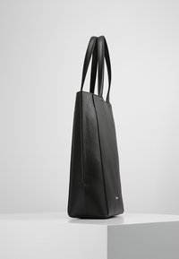 Czarna skórzana torba tote o prostokątnym kształcie, gładkiej fakturze i dwóch długich uchwytach; charakteryzuje się minimalistycznym designem i subtelnym logo.