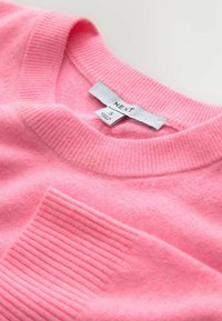 Svetlo roza pulover iz mehkega blaga, z rebrastim izrezom in poševnim rebrastim žepom. Oznaka velikosti S, vidna blagovna znamka.