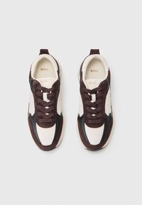 Baskets avec un dessus crème, des accents en daim marron foncé et des détails en cuir noir, design à lacets et logo imprimé sur la semelle intérieure.