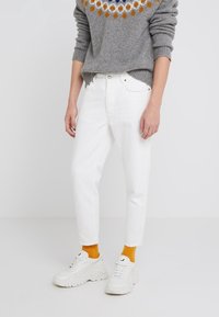 Vita denimjeans med rak passform, kombinerat med en grå stickad tröja med en färgglad cirkulär design och vita sneakers med orangea strumpor.