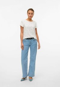 Letvægts hvid top med røde bladlignende mønstre, parret med lyseblå straight-leg jeans og blå spidse hæle.