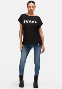 Camiseta negra de manga corta con estampados de personajes de dibujos animados en el pecho; combinada con jeans ajustados azules y botas negras con cordones.