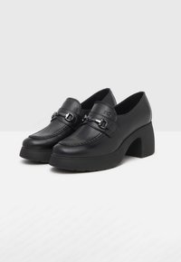 Black leather loafers with a low block heel, featuring decorative buckle hardware and contrasting stitching along the shoe's perimeter.