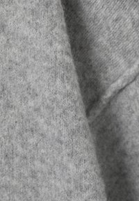 Tissu de pull en tricot gris clair présentant une surface douce et texturée avec des motifs de tricot variés et des nuances de couleur subtiles.