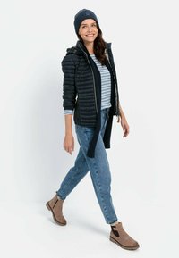 Zwarte pufferjack met capuchon, grijs gestreept topje, blauwe jeans en bruine chelsea boots. Inclusief beanie en zijritsdetails.