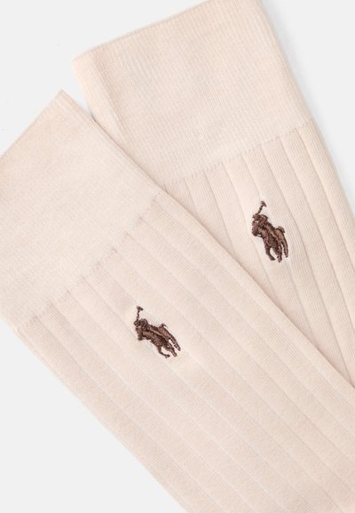 Bež sive nogavice s gladko teksturo, ki imajo na strani majhen rjav vezen logotip.