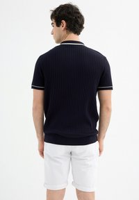 Polo de rayas acanaladas azul marino con mangas cortas, con franjas blancas en contraste a lo largo del cuello y los puños, combinado con pantalones cortos blancos enrollados.