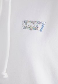 Vit hoodie med en holografisk Levi's-logotypapplikation, med en subtil textur och vit dragsko.