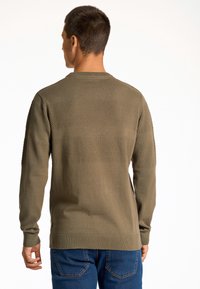 Maglione a maglia verde oliva con strisce orizzontali testurizzate, collo rotondo e maniche lunghe. Abbinato a jeans in denim blu.