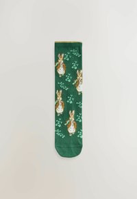Chaussettes vertes avec un motif répété de lapins bruns et blancs sur un fond texturé, agrémentées de petites fleurs. Matière en mélange de coton.