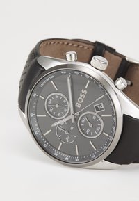 Montre chronographe avec un boîtier en acier inoxydable, un bracelet en cuir noir, un cadran gris foncé, trois sous-cadrans et un affichage de la date à 3 heures.