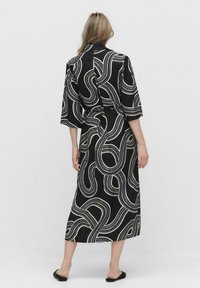 Czarna sukienka w stylu kimono z białymi spirującymi wzorami, z rękawami o długości trzech czwartych i talią ozdobioną paskiem, wykonana z gładkiego materiału.