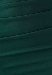 Tissu de robe vert foncé présentant des plis horizontaux, une texture lisse et une légère brillance, mettant en valeur une coupe ajustée.