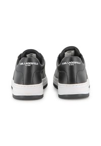 Sapatos de couro pretos com detalhes brancos, apresentando uma textura suave, forma arredondada e branding visível no calcanhar. Solado de borracha para tração.