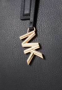 Schwarze, strukturierte Lederhandtasche mit einem glänzenden goldenen Zipper mit Zickzack-Design, befestigt an einem kurzen schwarzen Tragegurt.