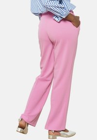 Roza krojena hlače iz mehkega materiala, z stranskimi žepi in naravnim vzorcem nog. Ujemajo se s srebrnimi sandalami na peto.