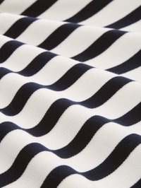 Svart-hvitt horisontalt stripet stoff folder seg og skaper bølgete tekstur med vekslende mørke og lyse bånd.