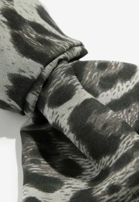 Czarna i szara tkanina o teksturze z wirującym wzorem. Materiał wydaje się miękki z delikatnym połyskiem i jest zebrany w węzeł.