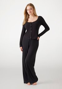 Black loungewear set featuring a long-sleeve, button-front top with a square neckline and loose-fitting pants. Soft, smooth texture.