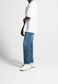 Camiseta blanca de algodón de manga corta, combinada con pantalones vaqueros de denim azul y zapatillas blancas. Estilo casual, corte relajado con un diseño de pierna recta.