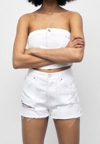 Shorts en denim blanc avec ourlet effiloché et détails usés. Présente une fermeture à bouton à l'avant et des poches arrière. Design de taille plate.