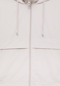 Lightweight white jacket with a zippered front, adjustable drawstrings, and a horizontal seam across the chest. Smooth texture, minimal design.