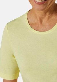 Kurzärmliges T-Shirt mit Rundhalsausschnitt aus weichem, hellgelbem Baumwollstoff. Sanfte Textur mit sichtbaren Nähten entlang des Halsausschnitts und der Ärmelkanten.