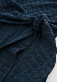 Námořnická strukturovaná látka s vlnitým vzorem, s detailem uzlu. Měkký materiál, který se elegantně splývá s jemným leskem.