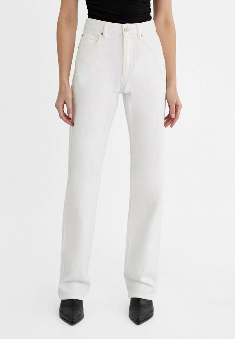 Pantaloni in denim bianco con vita alta, gamba dritta, design a cinque tasche e una sottile trama verticale, abbinati a scarpe nere a punta.