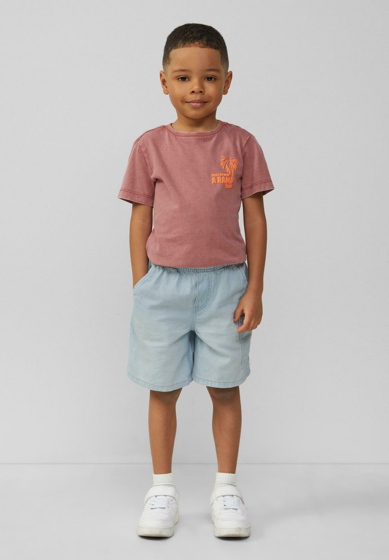 T-shirt rossa a maniche corte con grafica di palma, pantaloni corti azzurri e sneakers bianche, con polsini a coste e vita elastica.
