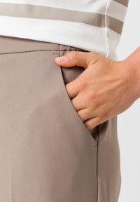 Beige broek van een gladde, gestructureerde stof. Hand gestoken in een zijzak, met een aansluitend ontwerp en minimale stiksel details.