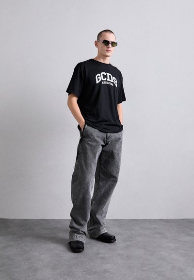 Maglietta nera con logo "GCDS", jeans grigi a gamba larga e zoccoli neri; tessuto morbido, vestibilità rilassata, dettaglio con zip laterale sui pantaloni.