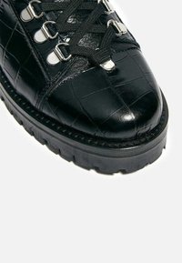 Stivale alla caviglia in pelle nera con texture a coccodrillo, punta rotonda, suola in gomma spessa e accessori metallici per i lacci.