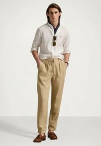 Lengva balta lino marškiniai, smėlio spalvos kelnės su raišteliu ir rudi slip-on batai. Papuošta akiniais nuo saulės ir mėlynos spalvos raštuotu kaklo šaliku.