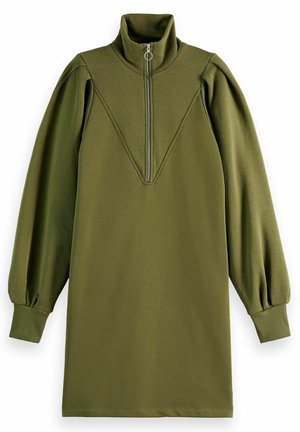 Woman wearing olive green long-sleeve mini dress with zipper collar, holding cream tote bag, and beige sneakers with white laces.