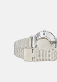 Silver mesh watch strap with a metallic clasp, featuring a round watch face with a polished silver case and a smooth texture.
