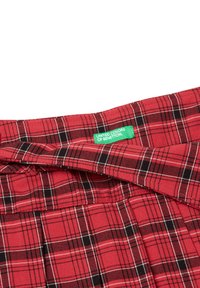 Tela de cuadro escocés rojo y negro con líneas blancas, con una etiqueta verde de United Colors of Benetton en la cintura.