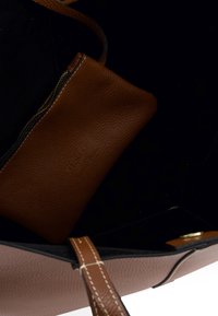 Brown leather pouch with zipper inside a black and light brown leather handbag with stitched handles and gold button closure.