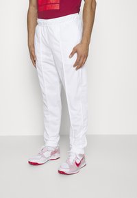 Witte sportbroeken met een elastische tailleband, voorzien van zijstrepen. Gepaard met rode en witte sportschoenen met mesh-details.