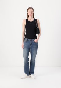 Schwarzes ärmelloses Tanktop mit dezentem Logo, hellblaue gerade Jeans, weiße Sneaker und eine kleine schwarze Umhängetasche.