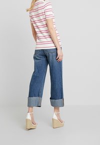 Camicia a maniche corte a righe bianca e rosa, abbinata a jeans larghi in denim. La modella indossa tacchi a spillo bianchi con dettagli intrecciati.