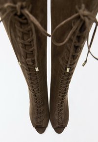 Paire de bottes hautes marron en cuir suédé à lacets, orteils ouverts et lacets noués vues de dessus sur fond blanc.