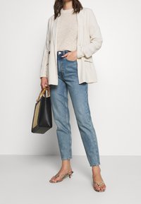 Blazer de lino beige, top de punto ligero, jeans azul de cintura alta, bolso negro con asas de bambú y sandalias metálicas con un pequeño tacón.