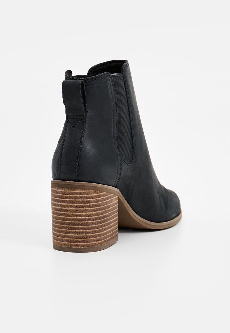 Zwarte leren enkellaars met een hoge blokhak, voorzien van een geribbeld design. Elastische zijpanelen voor gemakkelijke instap en een gladde, ronde neus.