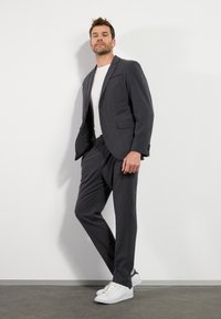 Grijze suit met een enkel-breasted blazer en plooibroek, gecombineerd met een wit T-shirt en witte sneakers. Glad stoffenafwerking.