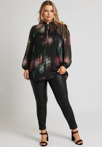 Blusa nera fluida con un motivo floreale in verde, rosa e viola, dotata di un collo alto, maniche lunghe e texture plissettata. Abbinata a leggings neri.