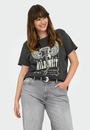 T-shirt gris foncé avec un graphique de guitare et d'ailes, comprenant du texte blanc et doré, associé à un jean gris clair et une ceinture noire studded.